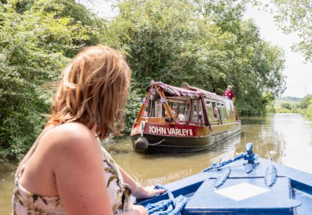 Woman on blue trip boat on Chesterfield Canal with red trip boat ahead