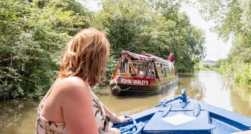 Woman on blue trip boat on Chesterfield Canal with red trip boat ahead