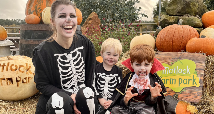 Woman and two children in halloween fancy dress smiling in front of pumpkins