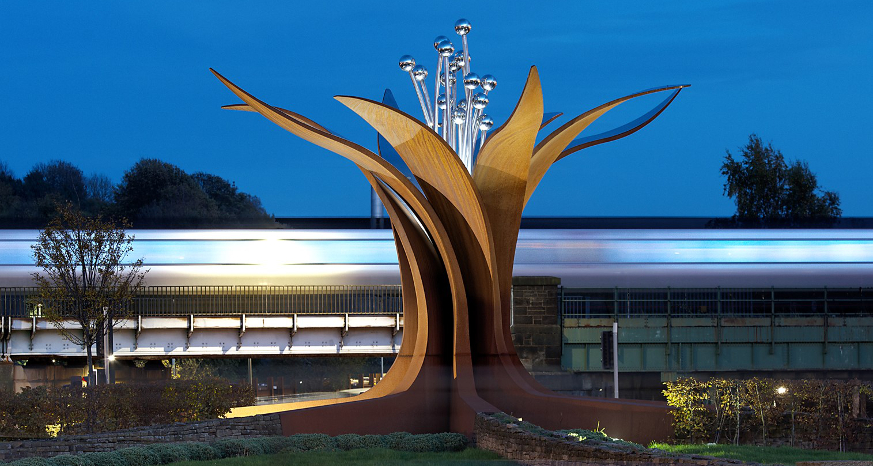Train passing behind the Growth sculpture at Hornsbridge Roundabout