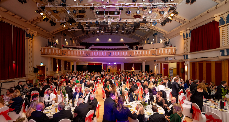 A full room of black-tie dressed guests at tables at the Winding Wheel Theatre, balcony and lighting above