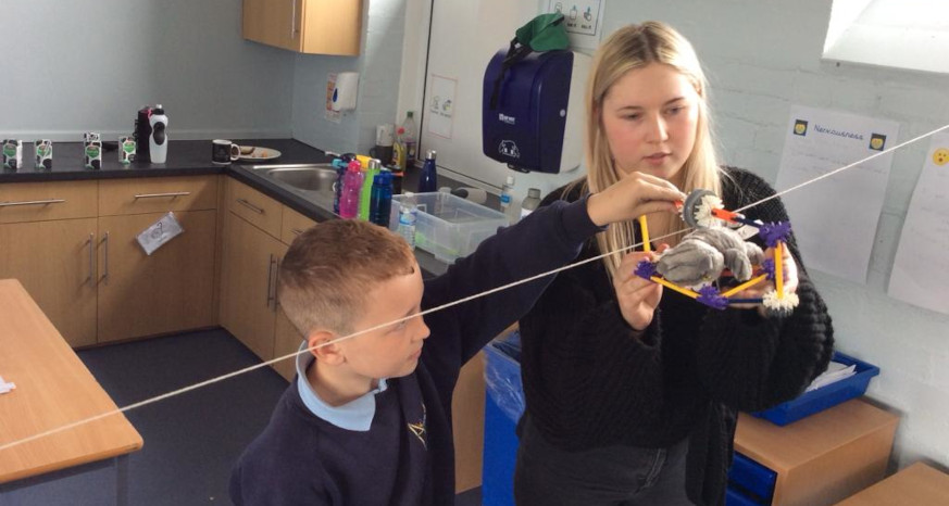 Woman with blonde hair and young boy attaching a model to a washing line in a classroom