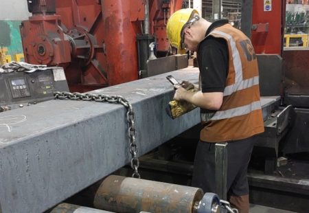 Man in orange high vis and yellow hard hat stood working with a steel bar