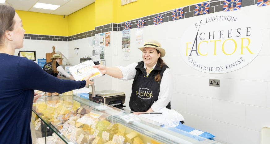 Cheese Factor female team member serving cheese in a paper bag to a female customer