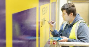 White male student painter painting purple text freehand on yellow wall