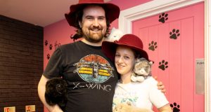 Male and female in red floppy hats hugging, cat toy on female's shoulder