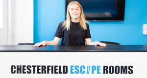 Female in black t-shirt stood behind branded Chesterfield Escape Rooms counter