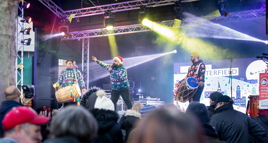 Two drummers and one singer all in Christmas jumpers and Santa hats on the big stage at Market Square, Chesterfield