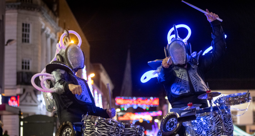 Two drummers in lit costumes, Crooked Spire and Christmas lights in background