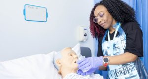 Black female student nurse wearing gloves giving drink to dummy