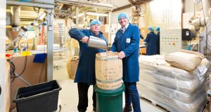 Two white males in hair nets and blue coats pouring coffee beans into a wooden barrel at Northern Tea Merchants