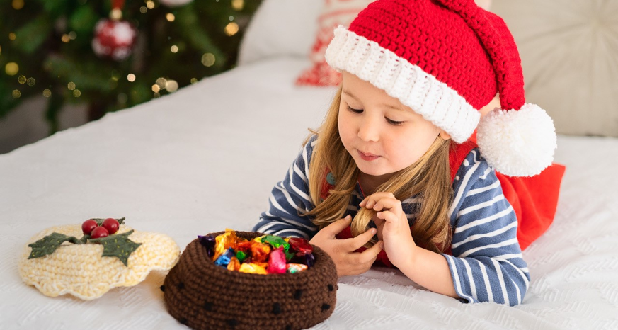 Young girl in Santa hat laying on front looking into a crocheted basket of chocolates 