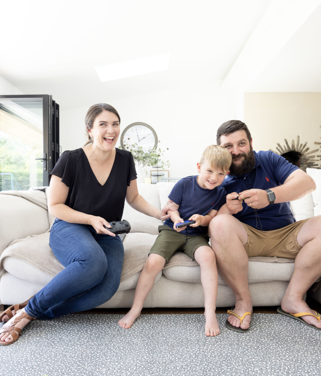 Mum and dad with son on sofa laughing and playing computer games