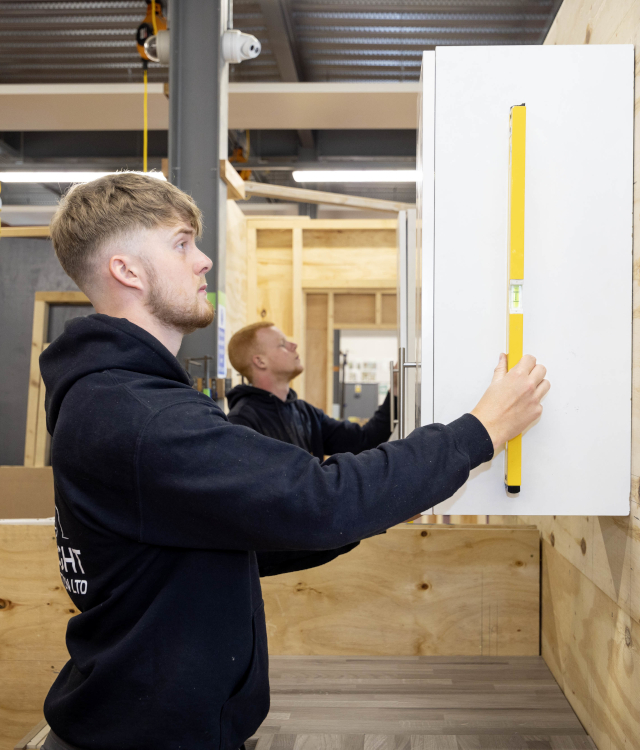 Young male measuring a cupboard door in the workshop at Chesterfield College