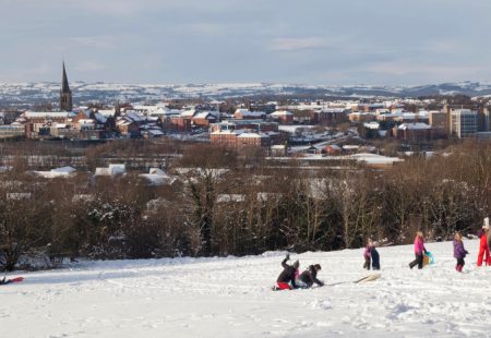 Children playing in snow at Tapton Park, Crooked Spire and houses in background