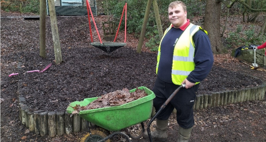 Young man standing in a playground with a wheelbarrow