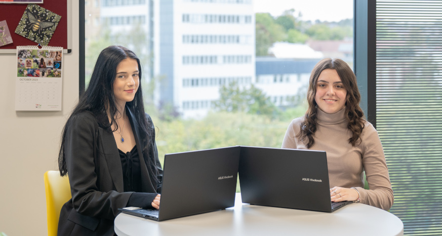 Two young women sitting at laptops in an office with a view out the window