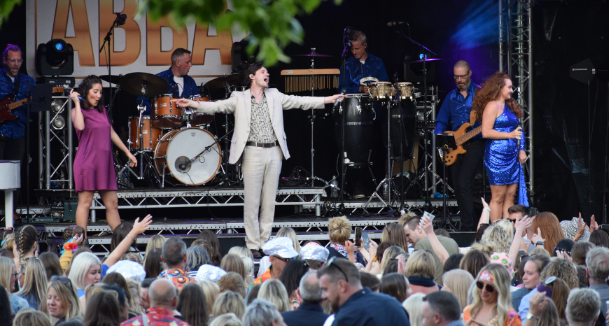 Man in white suit standing on an outdoor stage in front of a crowd