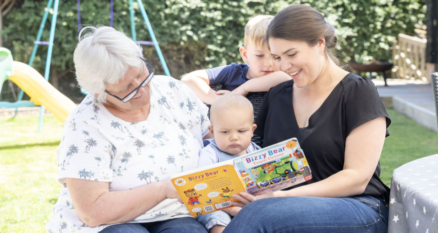 Grandma, mum and kids reading a book together in the garden