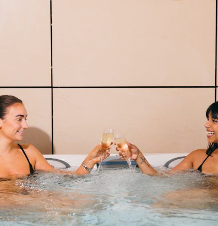 Two women in a hot tub with glasses of prosecco