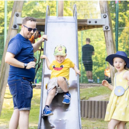 Man, woman and girl watching a boy go down a slide