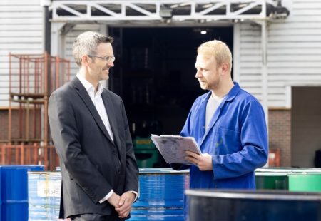 Business director in suit speaks with employee in overalls at manufacturing business