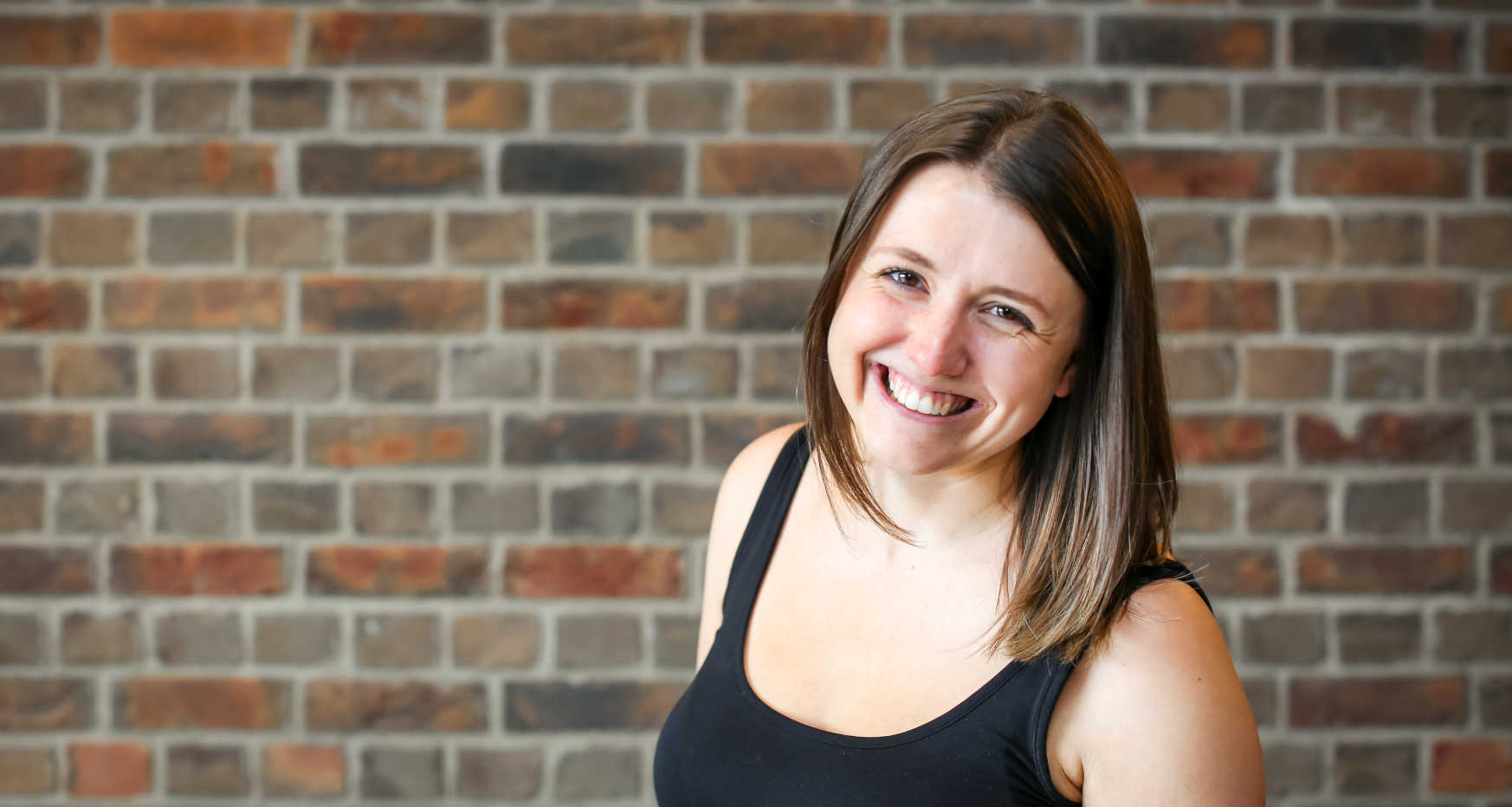 Female stood in front of brick wall smiling to the camera