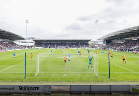 Photo of football match in stadium. Taken from behind a goal