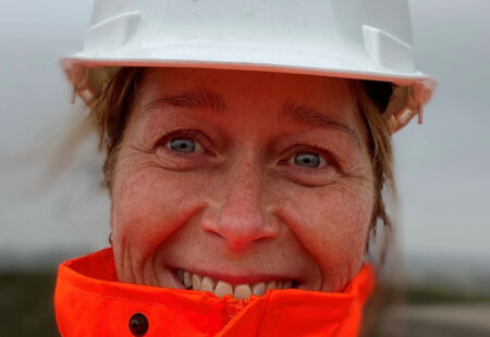 Close up of female in hard hat and orange high visibility jacket smiling to camera