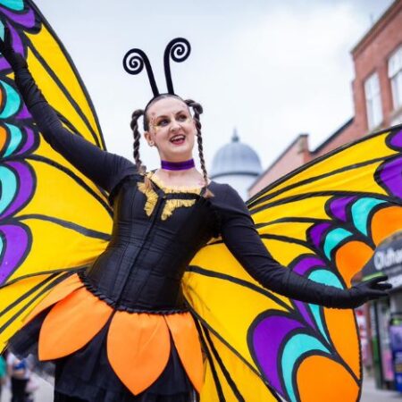 A street entertainer wearing large, colourful butterfly wings.