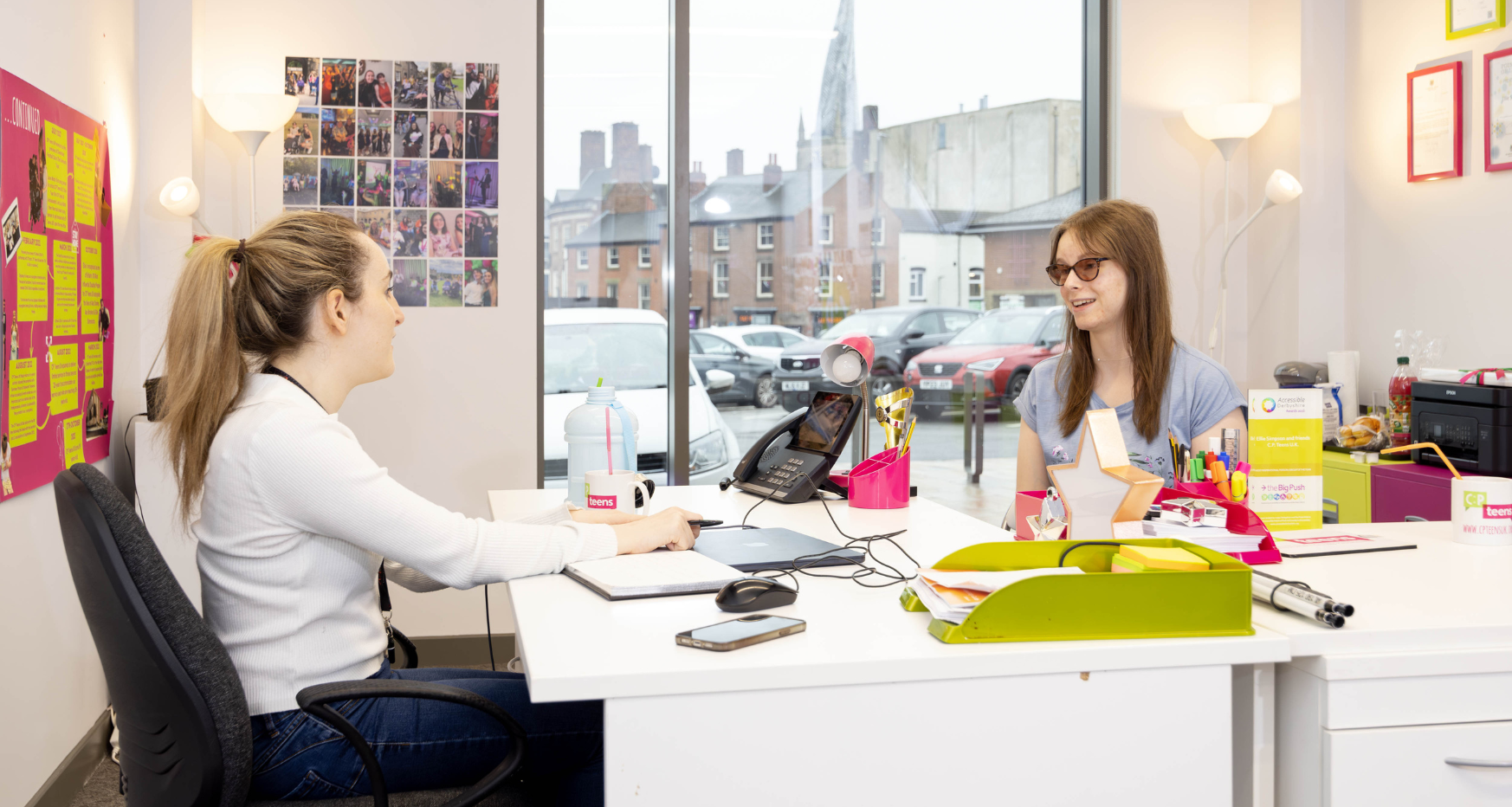 Two females working at computers in office, Crooked Spire in the background through office window