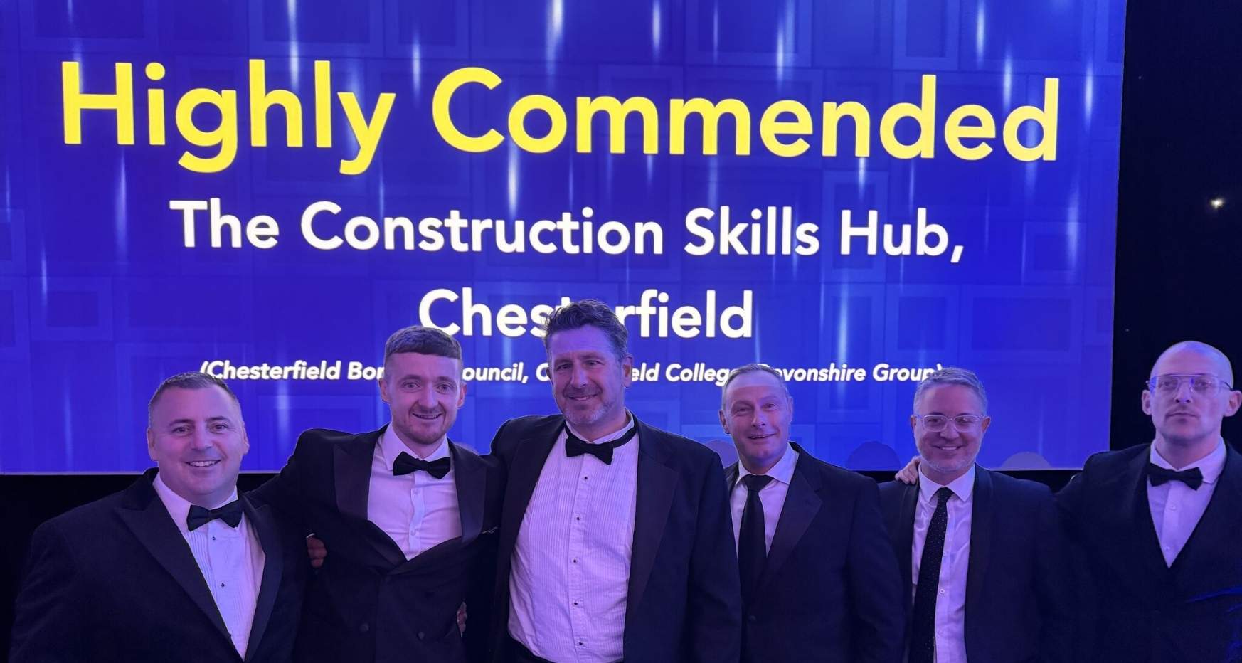 People stood in front of screen at East Midlands Property Awards. wording on screen Highly Commended The Construction Skills Hub, Chesterfield