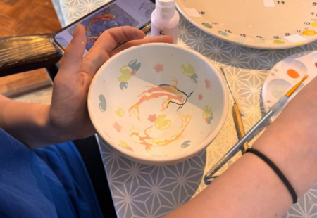 A clay bowl on a table with colourful paintings being applied to it.